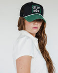 A woman wearing a white golf polo with a collar and a black hat with text on it.