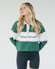 A woman wearing a long sleeve polo shirt with green, white, and pink colors, featuring the text 'Golfing Optional' on the front.