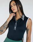 Woman wearing a black sleeveless Moore Polo with white collar and text details on a plain background