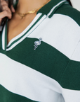 A woman wearing a green and white striped sweater with a V-neck collar and a small embroidered logo on the chest.