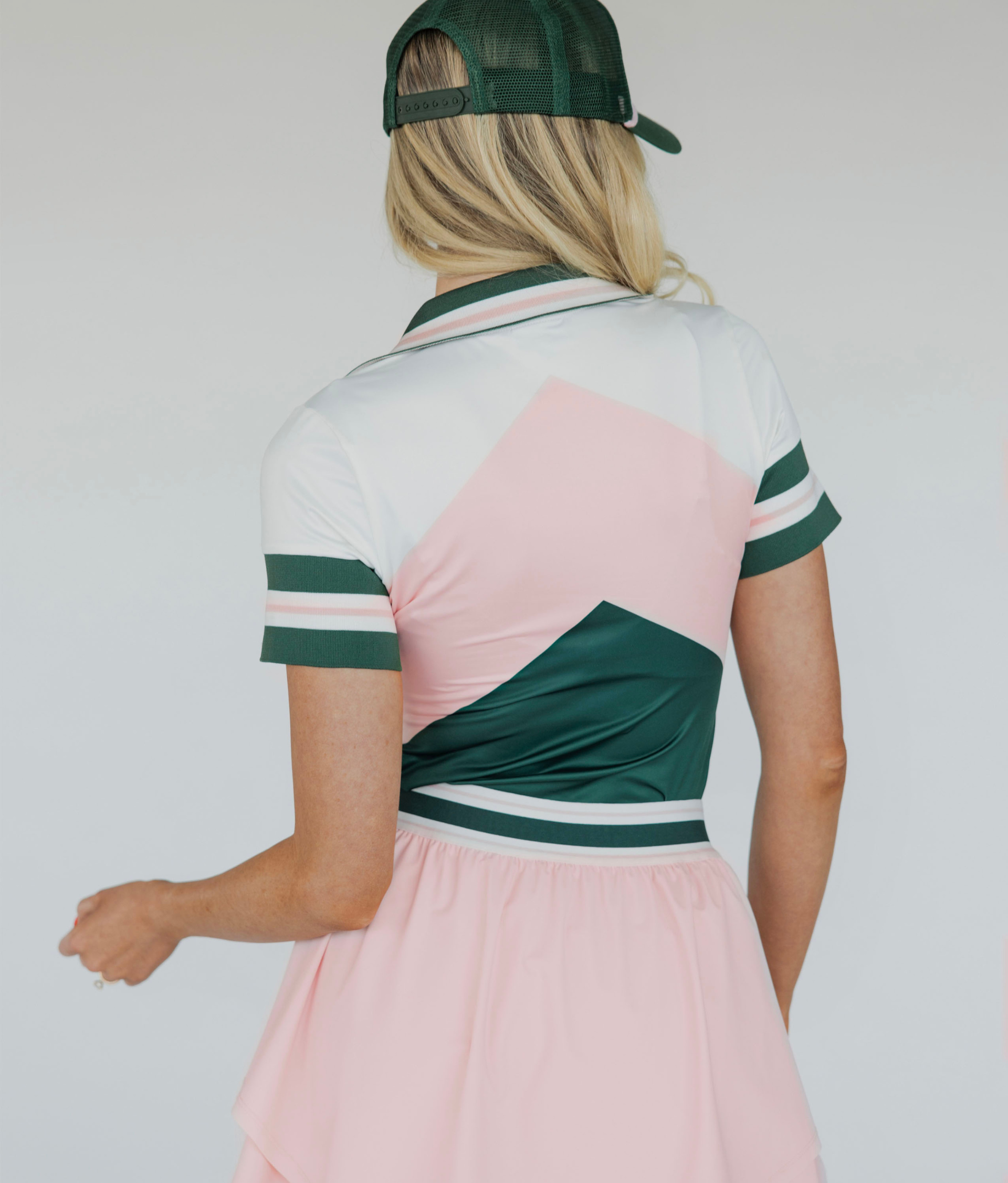 A woman wearing a pink and green Betty Polo shirt with chevron print and a preppy collar, paired with a light pink skirt.
