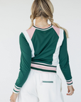 A female model wearing a green and white color-blocked crew neck golf shirt with long sleeves.