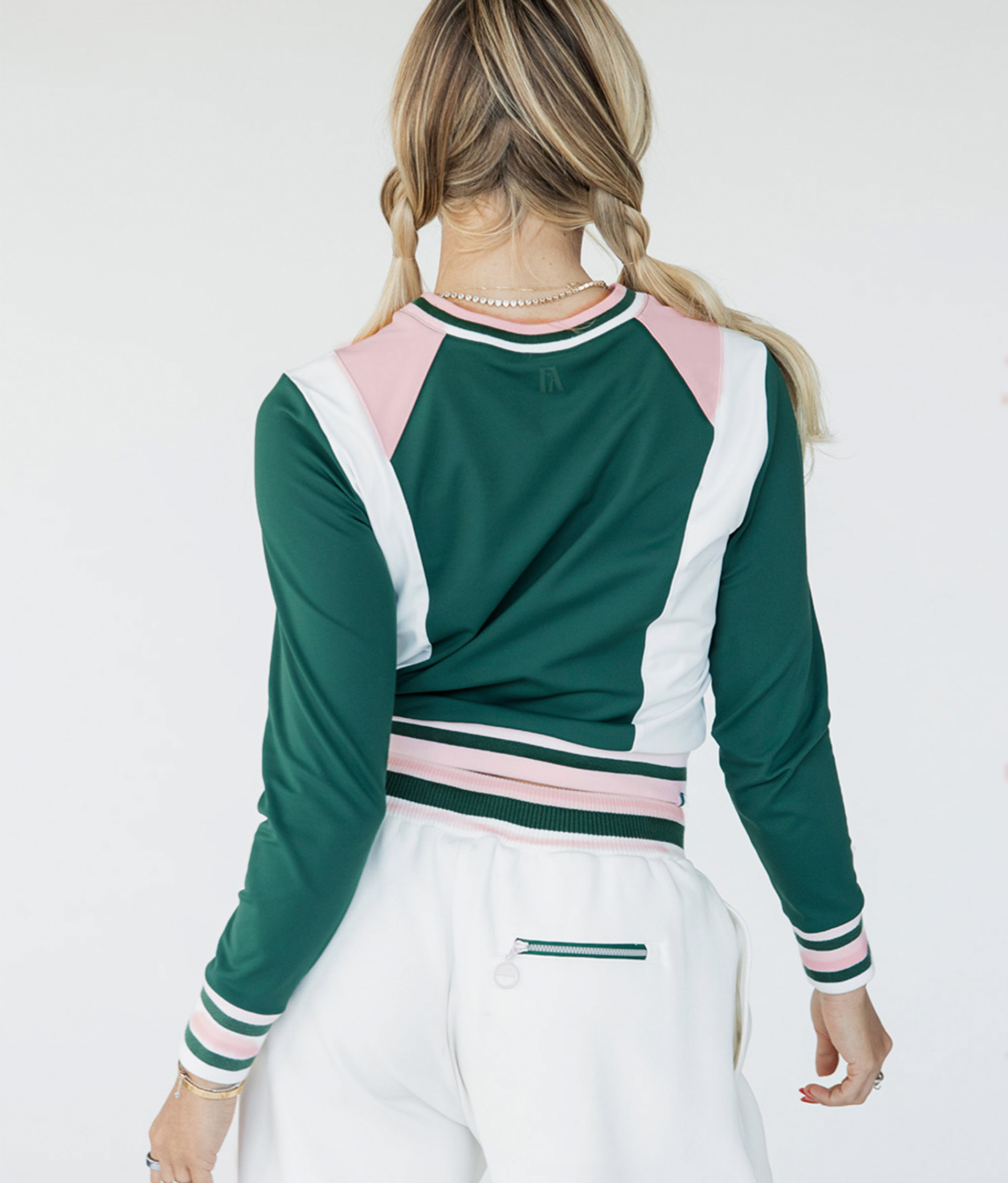 A female model wearing a green and white color-blocked crew neck golf shirt with long sleeves.
