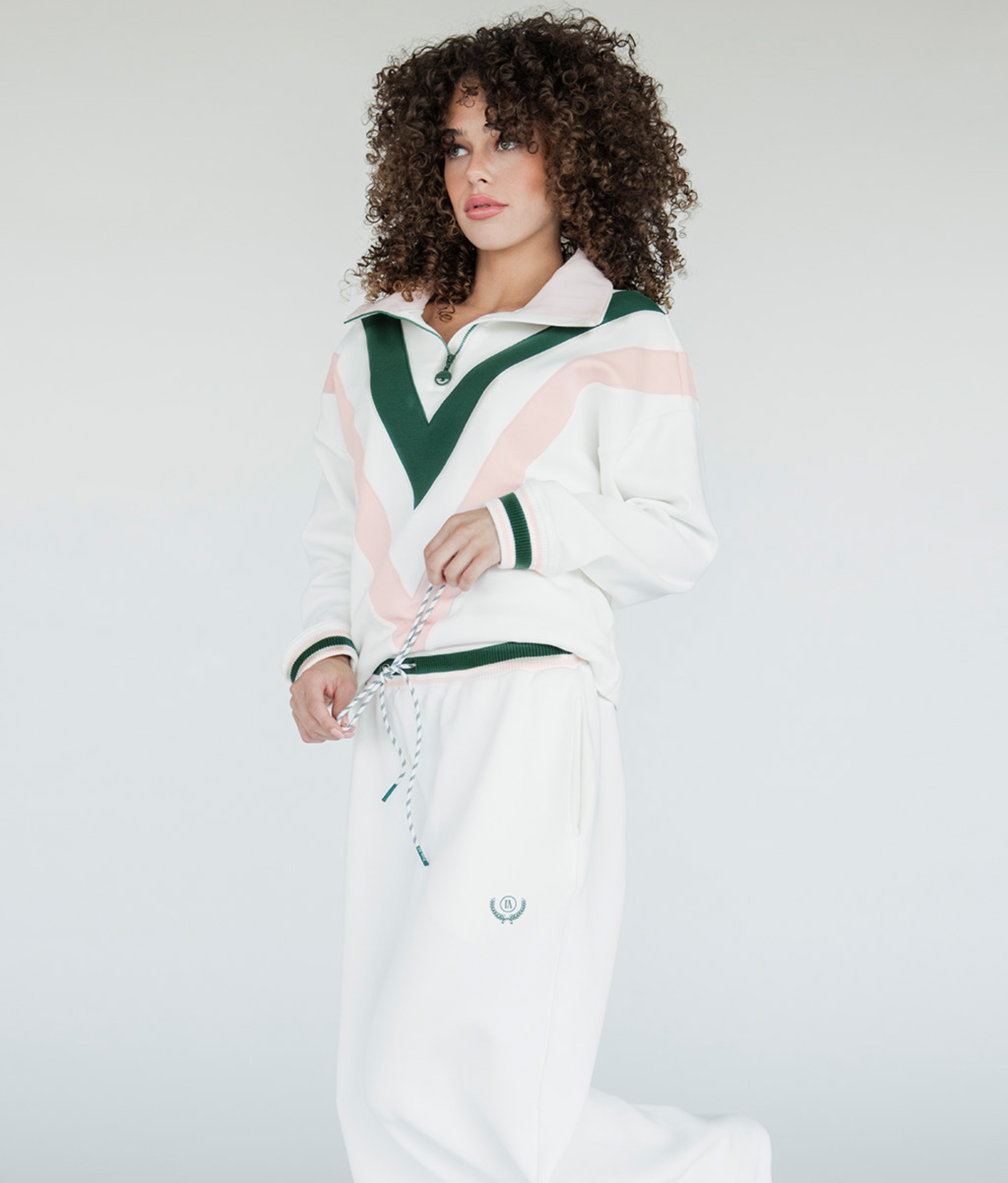 A woman wearing a white sweatshirt with pink and green geometric patterns and a quarter-zip design.