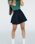 A person wearing a high-waisted black skirt with a green golf shirt. The skirt has side seam pockets and is made of a ribbed fabric.
