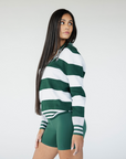 A woman wearing a green and white striped sweater with a V-neck collar and a small embroidered logo on the chest.