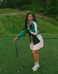 A female model wearing a black rain jacket with green sleeves, featuring a high neck, water-resistant properties, and a double zipper closure.
