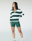 A woman wearing a green and white striped sweater with a V-neck collar and a small embroidered logo on the chest.