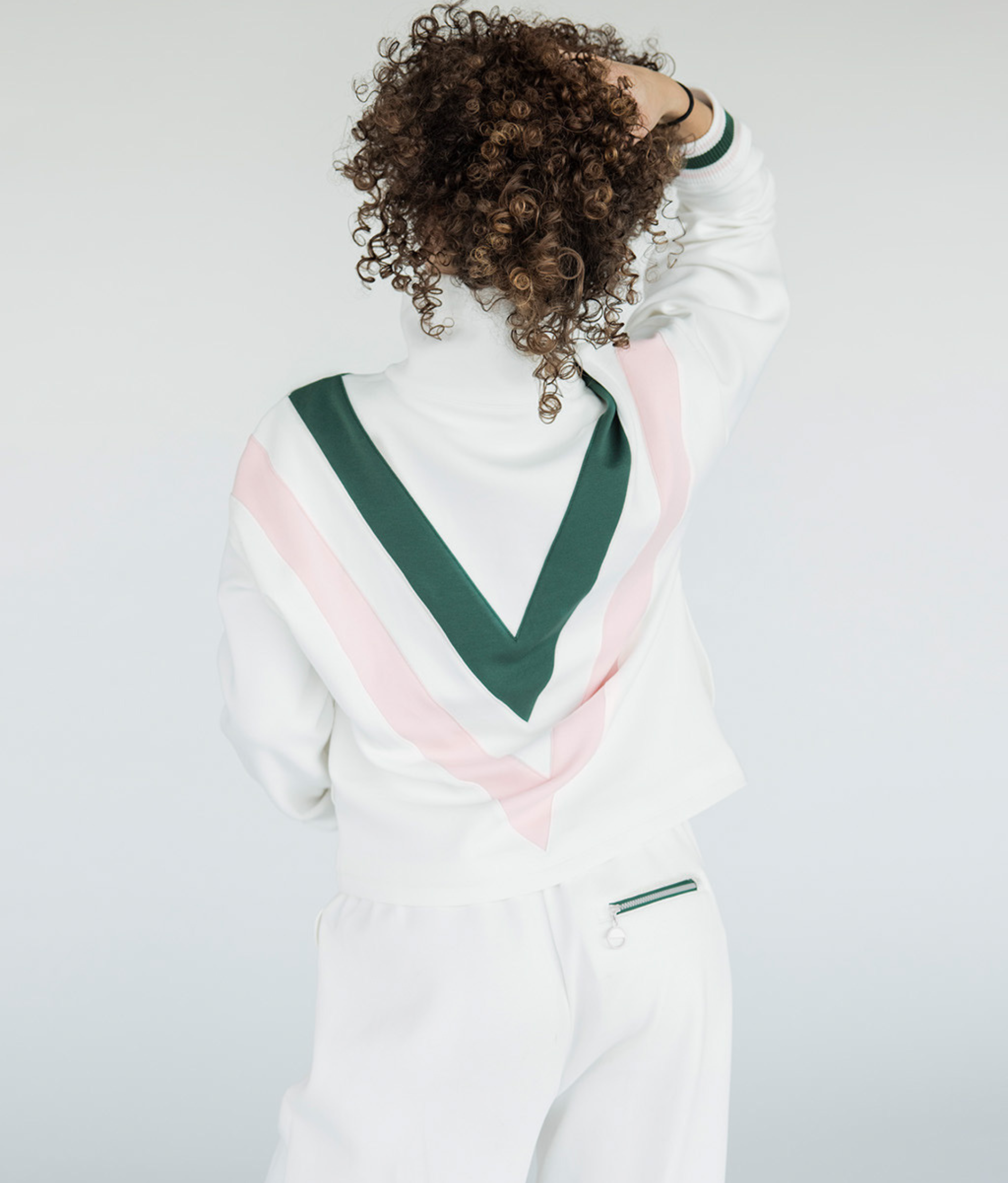 A woman wearing a white sweatshirt with pink and green geometric patterns and a quarter-zip design.
