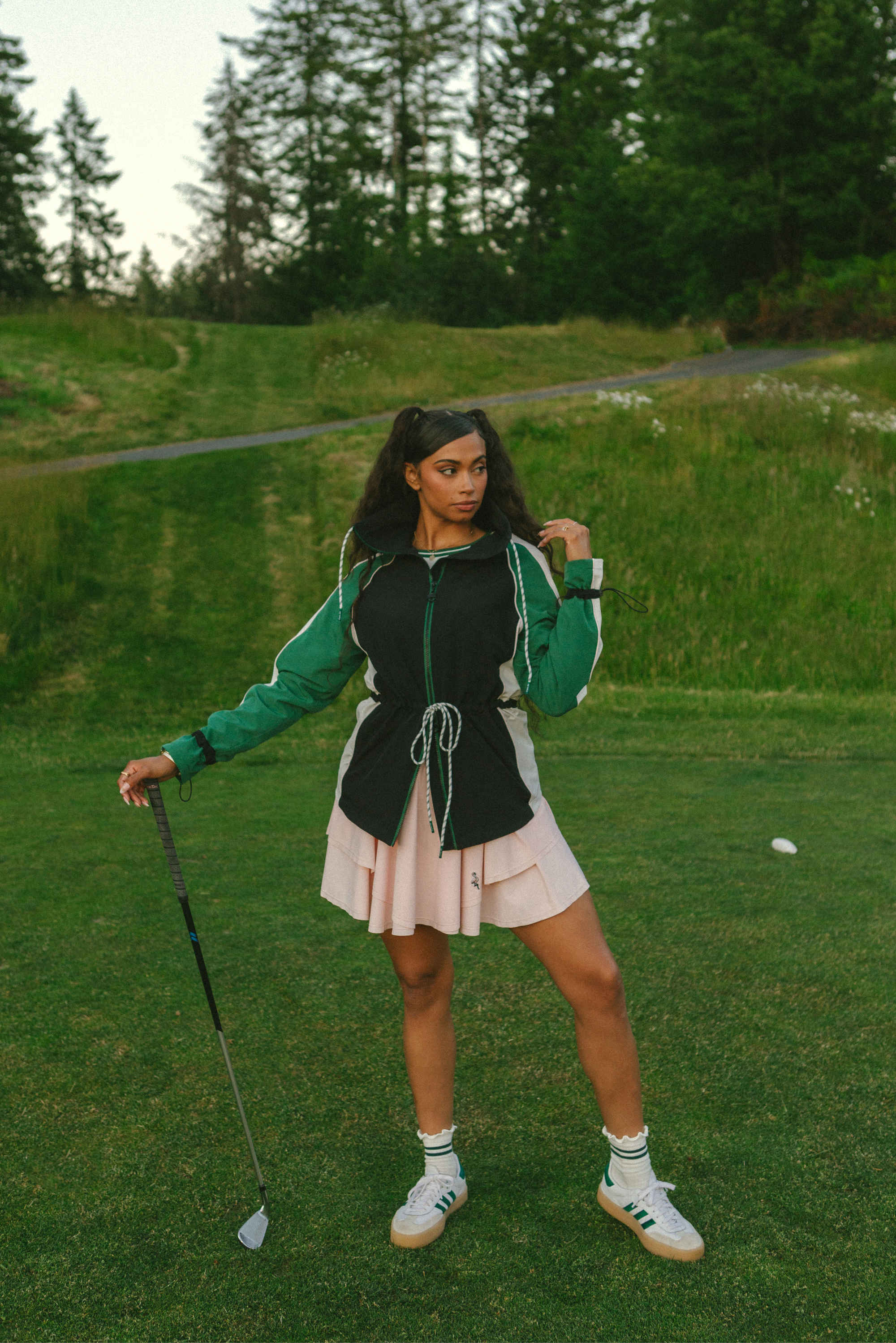 A female model wearing a black rain jacket with green sleeves, featuring a high neck, water-resistant properties, and a double zipper closure.