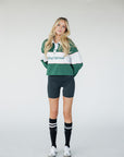 A woman wearing a long sleeve polo shirt with green, white, and pink colors, featuring the text 'Golfing Optional' on the front.