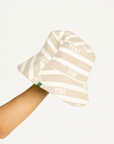 Beige and white striped bucket hat with 'FORE' branding held by a person on a white background