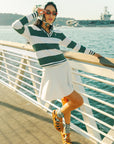 A woman wearing a green and white striped sweater with a V-neck collar and a small embroidered logo on the chest.