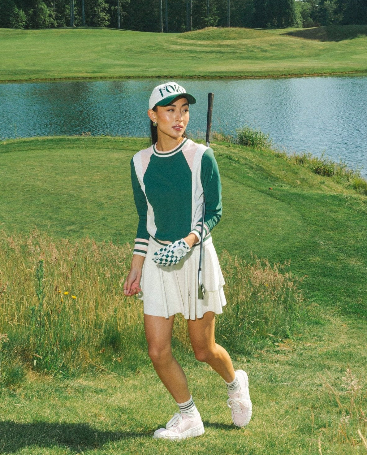 Woman on a golf course with a lake in the background wearing a green and white color-blocked crew neck golf shirt with long sleeves.