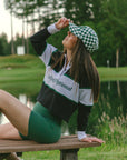 A person wearing a long sleeve polo shirt with horizontal green and white stripes and the text 'Golfing Optional' on the chest, paired with a green skirt.