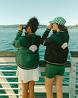 Two female models wearing a black and green bomber jacket with color-blocked sunset design on the back.