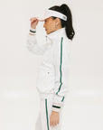 A woman wearing a white long sleeve golf jacket with green accents and a matching visor.