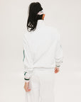 A woman wearing a white long sleeve golf jacket with green accents and a matching visor.
