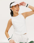 A woman wearing a white sleeveless tank top with a built-in bra, suitable for golfing, paired with white shorts and a visor.
