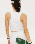 A woman wearing a white sleeveless tank top with a built-in bra, suitable for golfing, paired with white shorts and a visor.