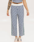 A person standing wearing the Bronson Pant in indigo color, which features a geometric pattern. The pants are casual and the person is paired them with a matching top and pink sneakers.