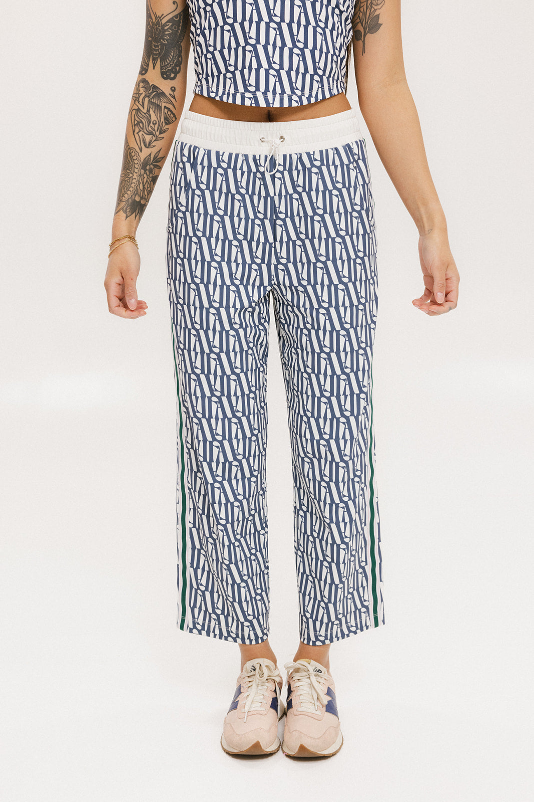A person standing wearing the Bronson Pant in indigo color, which features a geometric pattern. The pants are casual and the person is paired them with a matching top and pink sneakers.