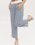 A person standing wearing the Bronson Pant in indigo color, which features a geometric pattern. The pants are casual and the person is paired them with a matching top and pink sneakers.