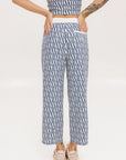 A person standing wearing the Bronson Pant in indigo color, which features a geometric pattern. The pants are casual and the person is paired them with a matching top and pink sneakers.