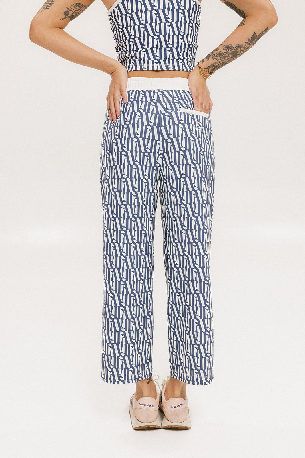 A person standing wearing the Bronson Pant in indigo color, which features a geometric pattern. The pants are casual and the person is paired them with a matching top and pink sneakers.