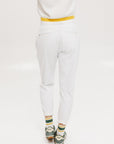 A person wearing white athletic pants and a white t-shirt with yellow details, standing against a white background.