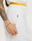 A person wearing white athletic pants and a white t-shirt with yellow details, standing against a white background.