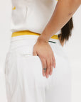 A person wearing white athletic pants and a white t-shirt with yellow details, standing against a white background.