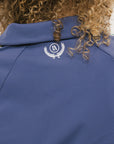 A woman is wearing a blue jacket with a white zipper and green stripes on the sleeves and pants. The jacket has a collared neckline.
