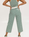 A pair of green checkered pants with a relaxed fit and pockets, worn by a model in a matching checkered top and sneakers.
