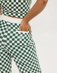 A pair of green checkered pants with a relaxed fit and pockets, worn by a model in a matching checkered top and sneakers.