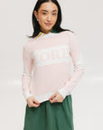 A woman wearing a pink fore all Fore Sweater with white accents and a green skirt.