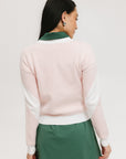 A woman wearing a pink fore all Fore Sweater with white accents and a green skirt.