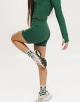 A pair of green mid-rise shorts with a logo on the left leg, worn with a matching green crop top, white sneakers, and checkered socks.