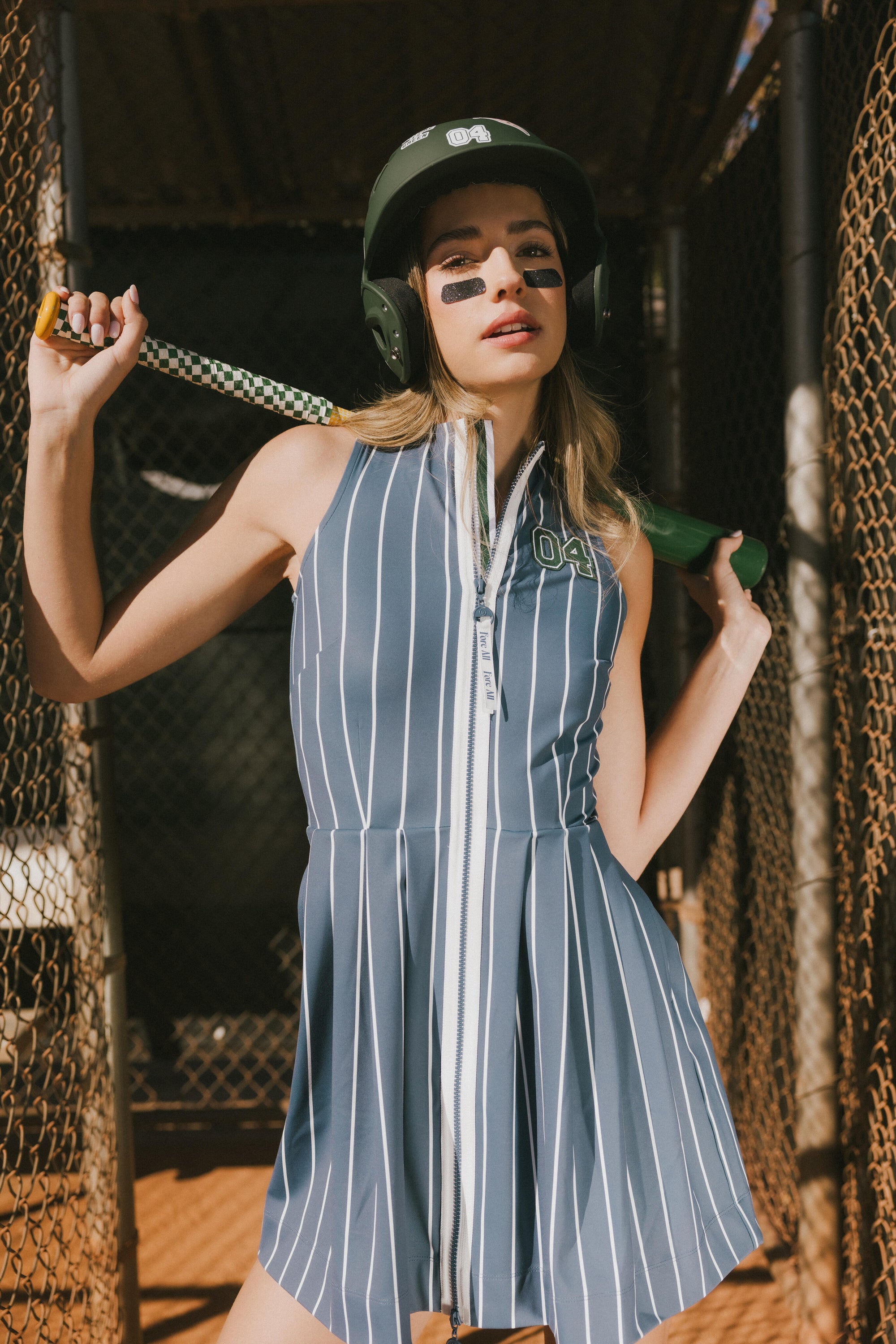 A woman is wearing a sleeveless, pleated, pinstripe indigo dress with a halter neck, side seam pockets, and a full-length two-way zipper at the center front.