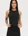 A smiling woman wearing a black tank top with a built-in bra, posing against a white background.