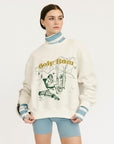 Person wearing a white sweater with graphic design and text, standing against a plain background