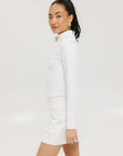 A woman wearing a white long sleeve golf top with a mock neckline.
