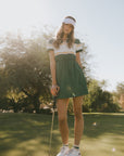 Woman on a golf course holding a golf club with trees in the background