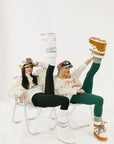 Two people sitting on chairs with one person lifting a large cylindrical object, all wearing casual outfits.