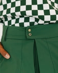 Person wearing a green skort and checkered top on a white background