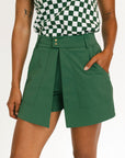 Person wearing a green skort and checkered top on a white background