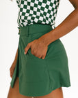 Person wearing a green skort and checkered top on a white background