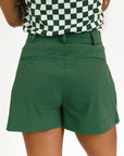 Person wearing a green skort and checkered top on a white background