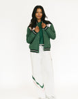 Person wearing a green varsity jacket and white pants on a white background