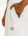 White pants with a green logo on the leg, worn by a person.
